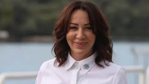 Pjevačica Romana Panić nasmijana u bijeloj košulji na otvorenom prostoru.