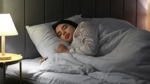 Žena mirno spava u krevetu pored upaljene noćne lampe