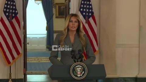 Melania Trump stoji za govornicom s američkim zastavama u pozadini.