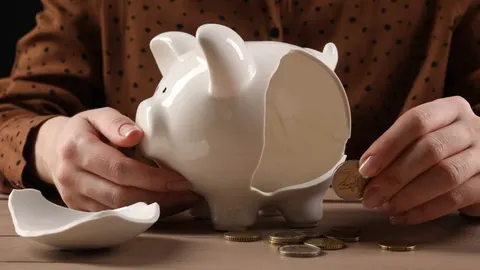 Razbijena bijela keramička kasica prasica u obliku svinje i kovanice eura na stolu.