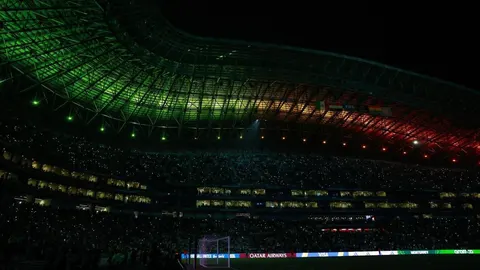 Moderni nogometni stadion s osvijetljenim krovom i prepunim tribinama noću.