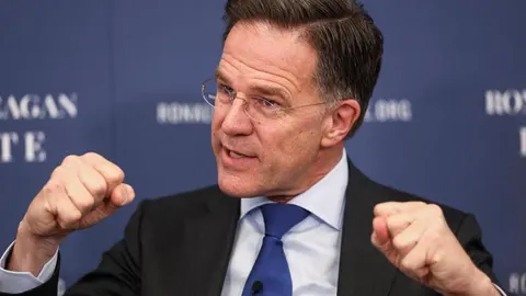 Mark Rutte s naočalama u odijelu gestikulira stisnutim šakama tijekom govora.