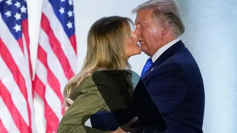 Donald i Melania Trump u bliskom trenutku ispred američkih zastava.