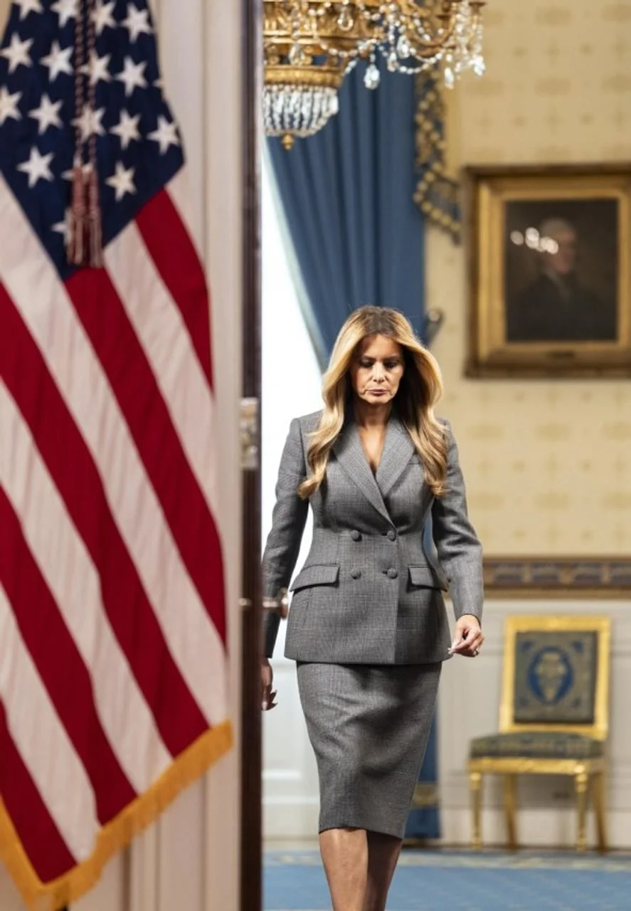 Melania Trump u sivom kostimu prolazi pored američke zastave