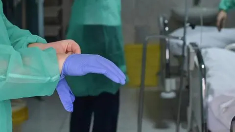 Medicinski radnik u zelenoj odori navlači plavu nitrilnu rukavicu u bolnici.