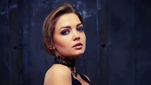 Portret žene s ozbiljnim izrazom lica ispred tamne pozadine.