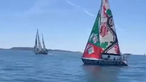 Jedrenjak s oslikanim jedrima plovi na otvorenom moru pod plavim nebom.