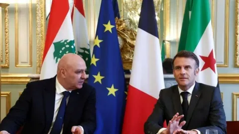 Emmanuel Macron i libanonski dužnosnik sjede ispred zastava Francuske, EU-a i Libanona.