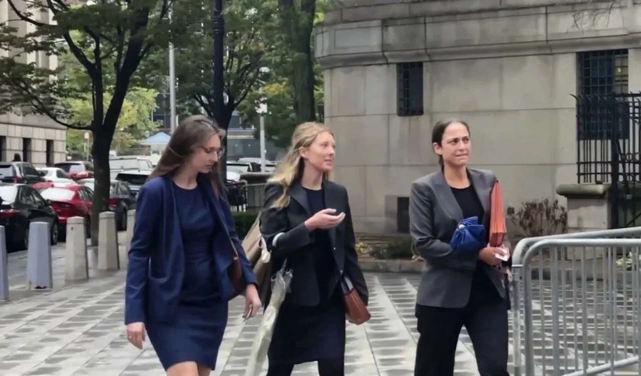 Tri žene u poslovnim odijelima hodaju pločnikom ispred kamene zgrade.