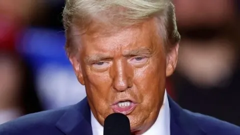 Donald Trump govori na mikrofon s ozbiljnim izrazom lica tijekom javnog nastupa.