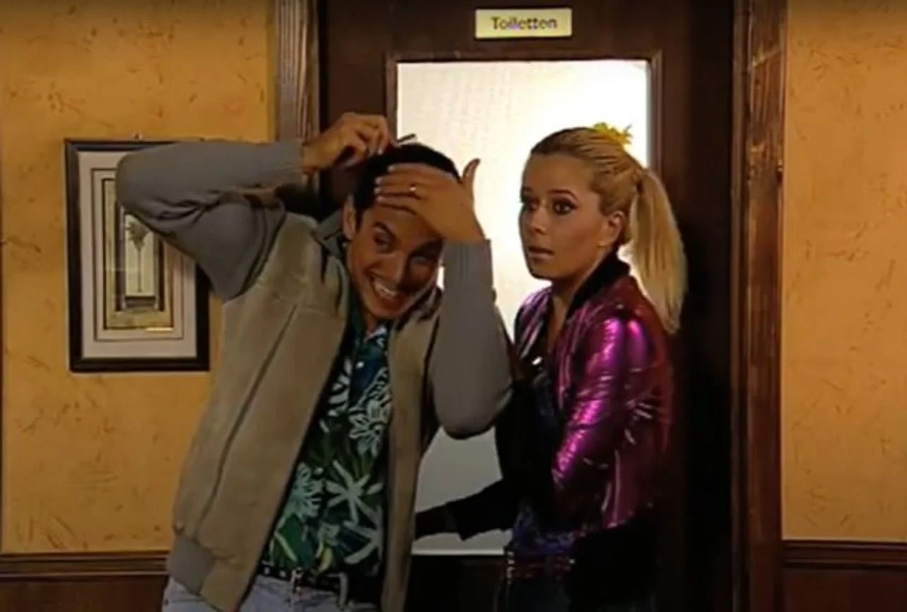 Voditeljica Emilija Bunjac u ljubičastoj jakni stoji pored kolege u televizijskom studiju.