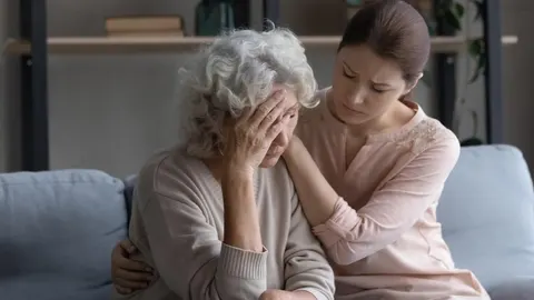 Mlađa žena tješi zabrinutu stariju ženu s bijelom kosom na kauču.