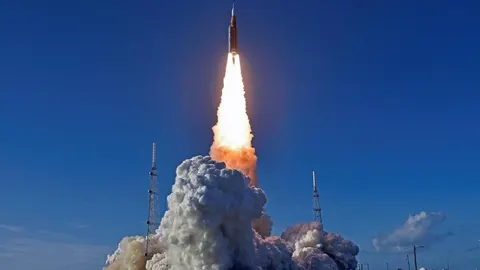 Lansiranje svemirske rakete s velikim oblakom dima pod vedrim plavim nebom.