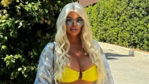 Dara Bubamara s plavom kosom i sunčanim naočalama stoji ispred zelenila.