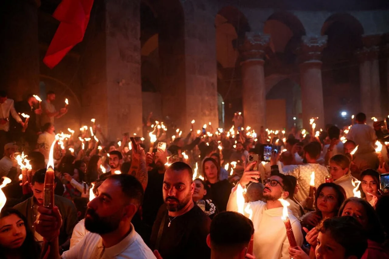 Ljudi u kamenoj bazilici drže snopove upaljenih svijeća i snimaju mobitelima
