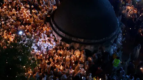 Mnoštvo vjernika u bijeloj odjeći drži upaljene svijeće oko male kupole