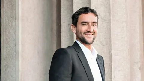 Marin Čilić u crnom odijelu i bijeloj košulji smiješi se ispred kamenih stupova.