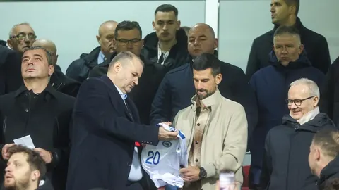 Novak Đoković prima bijeli sportski dres s brojem 20 na tribinama.