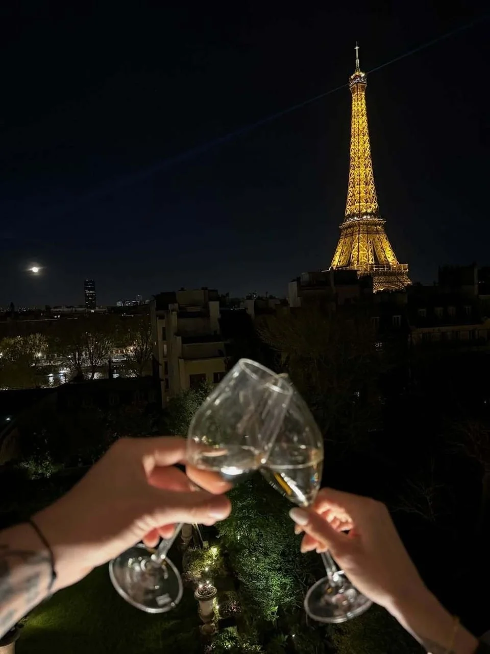 Dvije čaše šampanjca u prvom planu s osvijetljenim Eiffelovim tornjem noću.