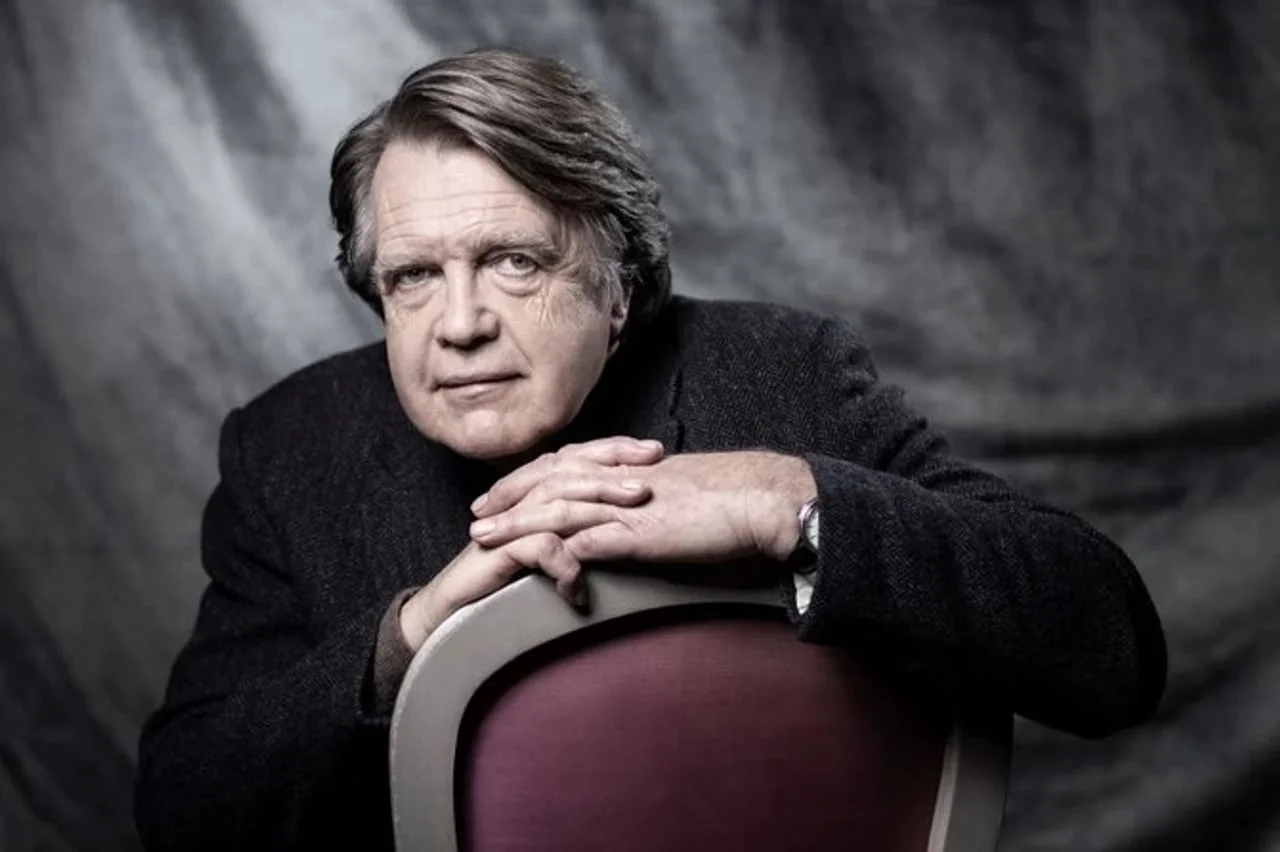 Merlin Holand naslonjen na stolicu gleda u kameru