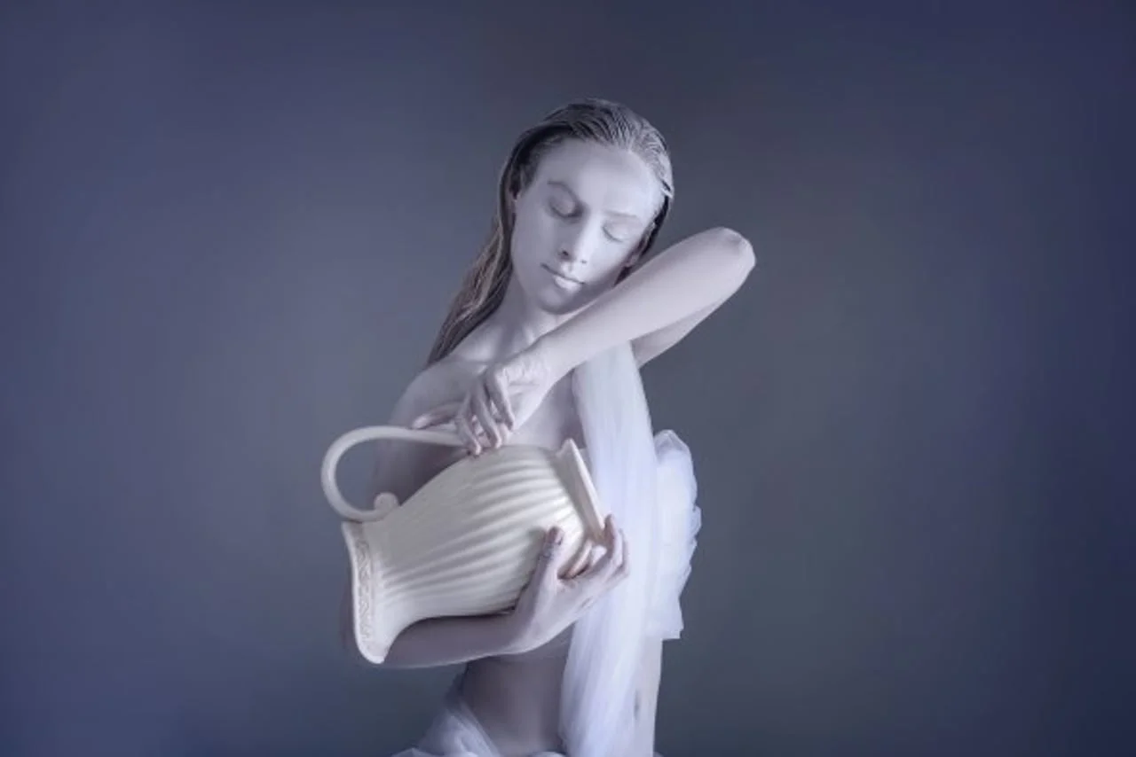 Žena prekrivena bijelom bojom drži keramički vrč u umjetničkoj pozi