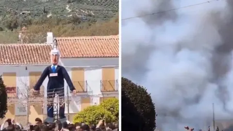 Velika figura muškarca u odijelu ispred zgrade i gusti bijeli dim nakon eksplozije.