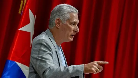 Miguel Díaz-Canel govori ispred kubanske zastave i crvene zavjese.