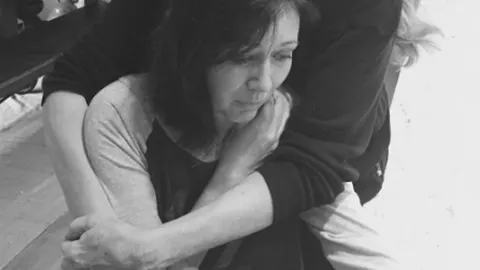 Crno-bijela fotografija Shannen Doherty koju netko grli s leđa