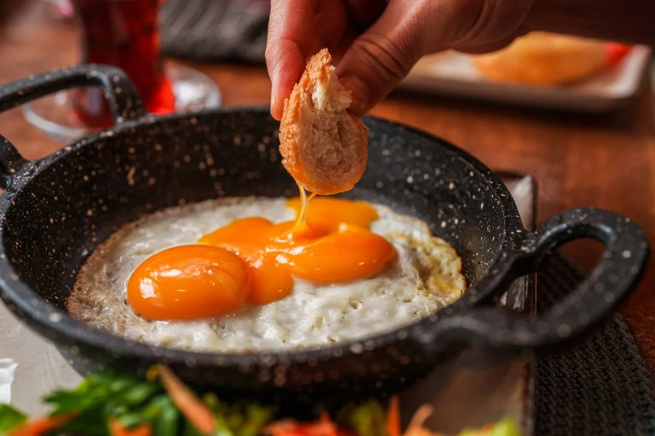 Pržena jaja u tavi s komadom kruha koji se umače u mekani žumanjak.