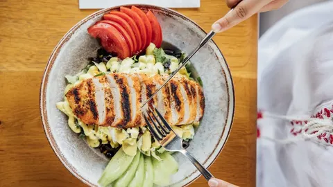 Pečena piletina poslužena uz svježu salatu od rajčice i krastavaca na tanjuru.