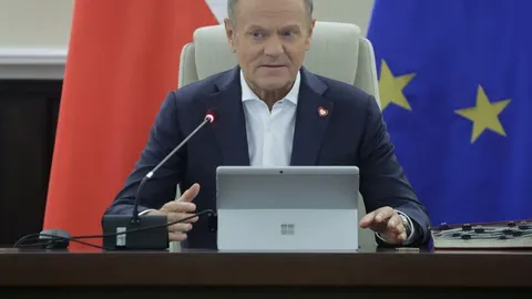Donald Tusk sjedi za stolom ispred poljske i europske zastave