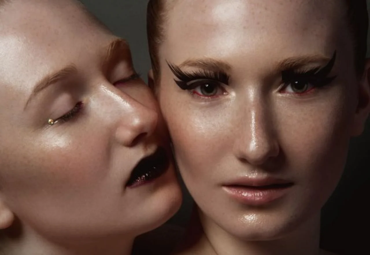 Krupni plan dviju žena s naglašenom šminkom i tamnim usnama.