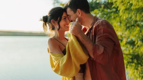 Nasmijani par pleše zagrljen uz obalu jezera u sumrak.