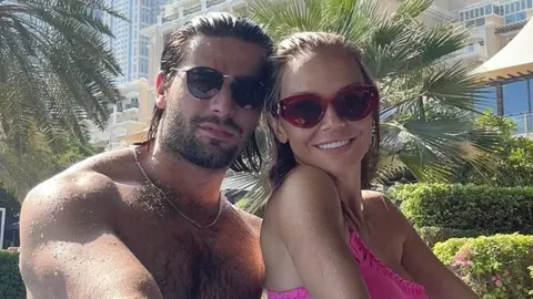 Maja Šuput i Šime Elez poziraju sa sunčanim naočalama ispred palmi i zgrade.