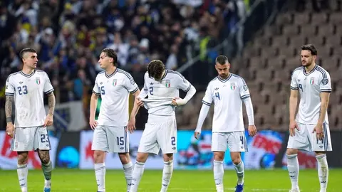 Talijanski nogometaši u bijelim dresovima stoje na terenu pognutih glava.