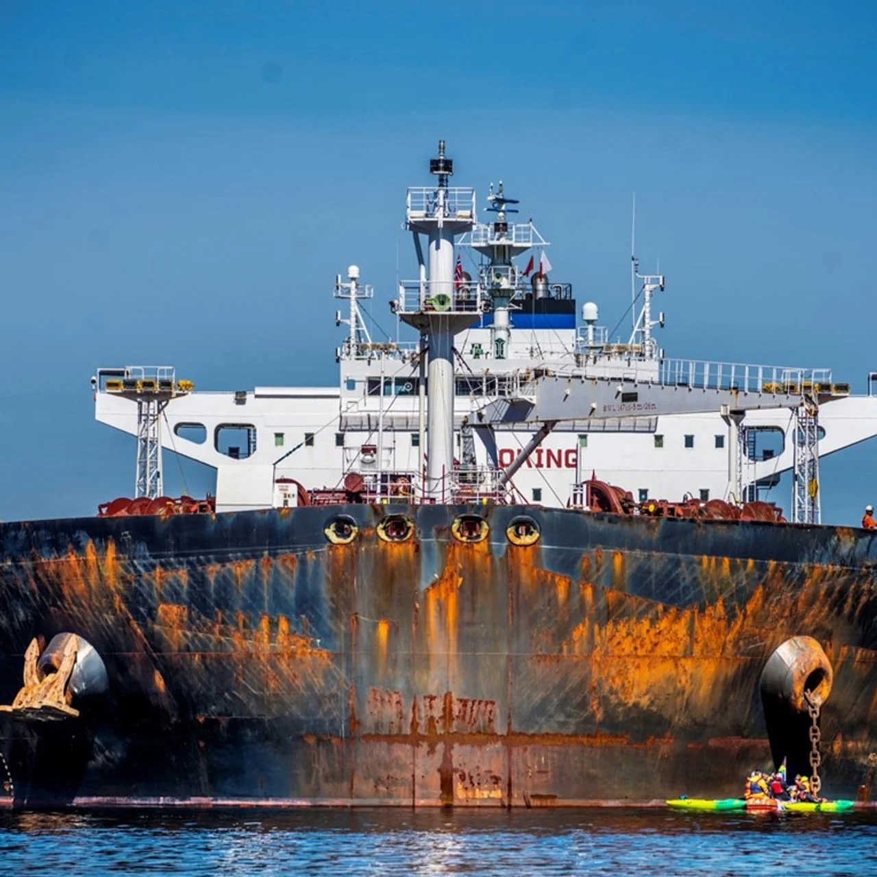 Veliki zahrđali teretni tanker na moru s malim čamcima u podnožju.