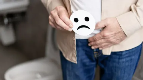 Muškarac drži papirnati tužni emotikon ispred donjeg dijela trbuha