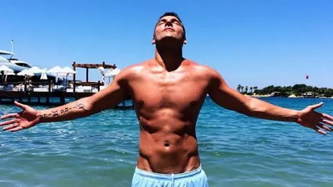 Duško Tošić stoji raširenih ruku u plitkom moru pod suncem.