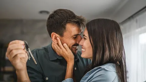 Nasmijani mladi par u zagrljaju dok muškarac drži ključeve u ruci.