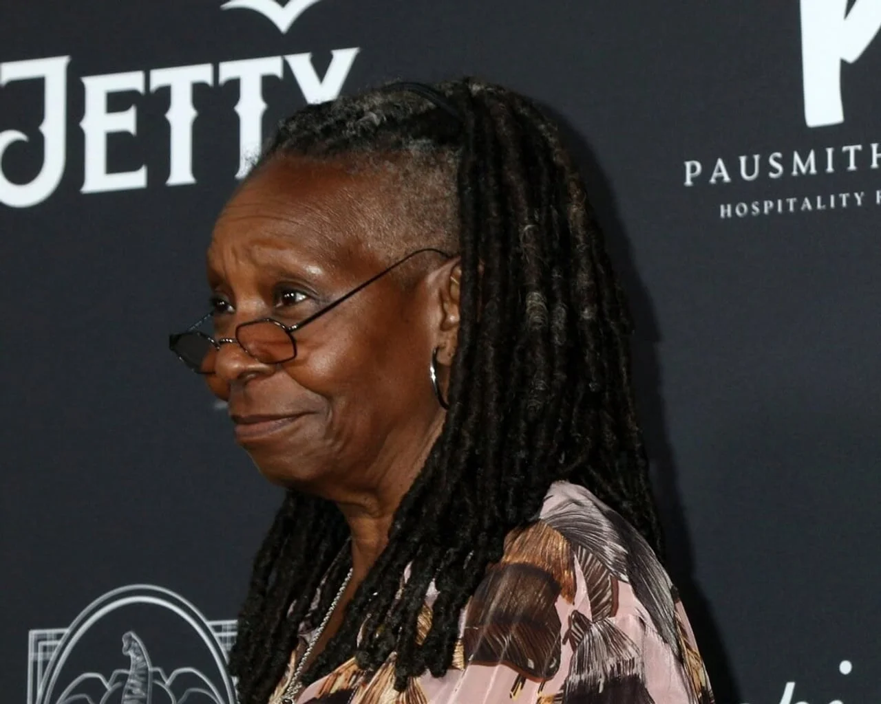 Portret Whoopi Goldberg iz profila s naočalama i dredovima.