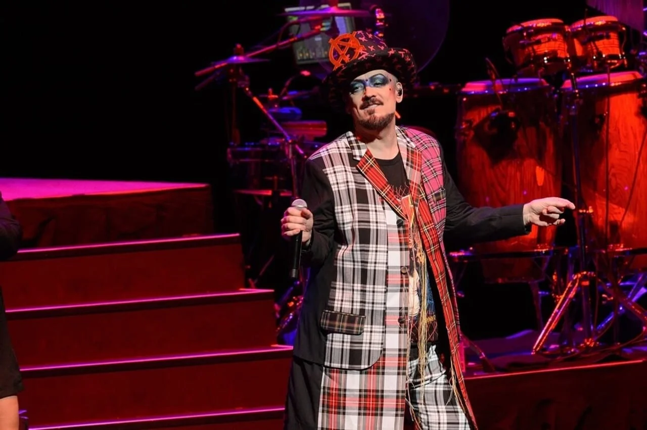 Boy George nastupa na pozornici u kariranom odijelu i sa šeširom.