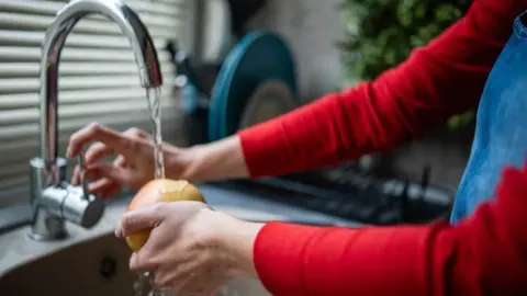 Osoba pere jabuku pod mlazom vode u kuhinjskom sudoperu