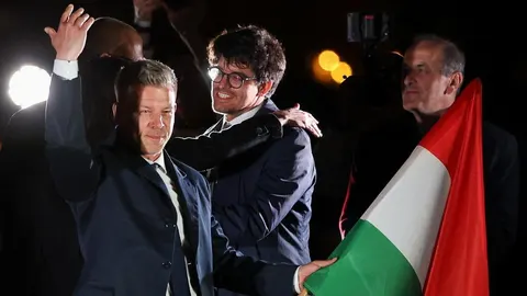 Péter Magyar maše okupljenima dok drži mađarsku zastavu na pozornici.