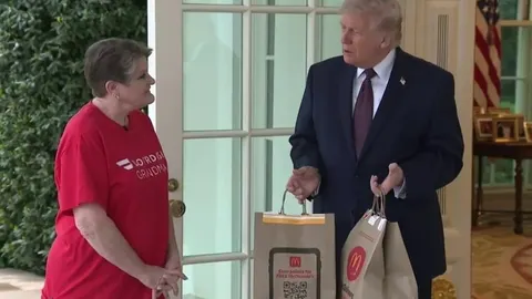 Donald Trump stoji ispred vrata Bijele kuće i drži vrećice s hranom pored dostavljačice.