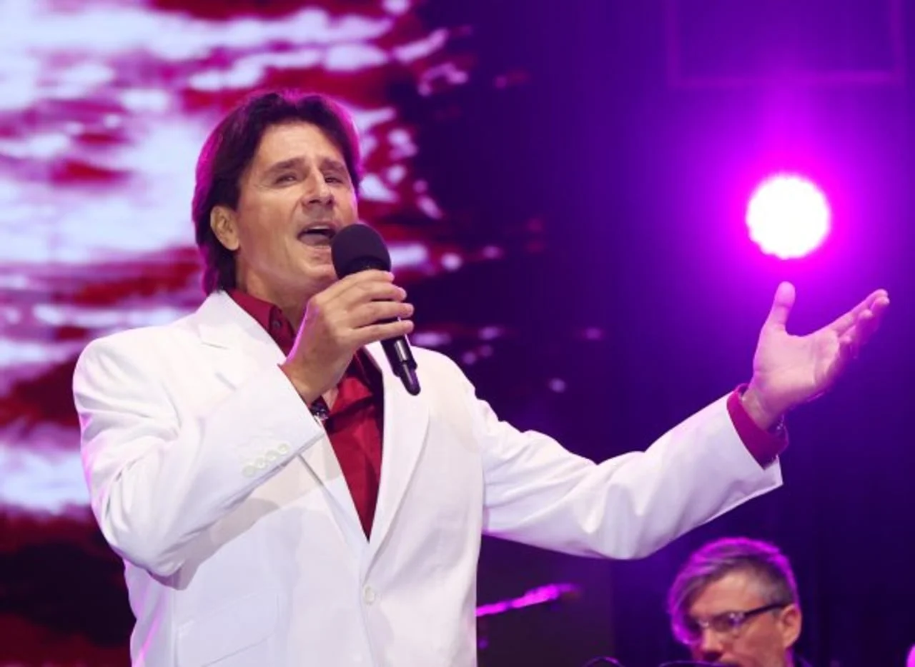 Amir Kazić Leo pjeva na pozornici u bijelom odijelu s Mikrofonom u ruci.