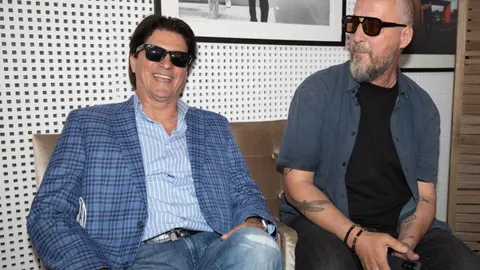 Amir Kazić Leo u plavom kariranom sakou sjedi i smije se s kolegom.