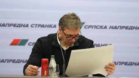 Aleksandar Vučić čita dokumente ispred logotipa Srpske napredne stranke.
