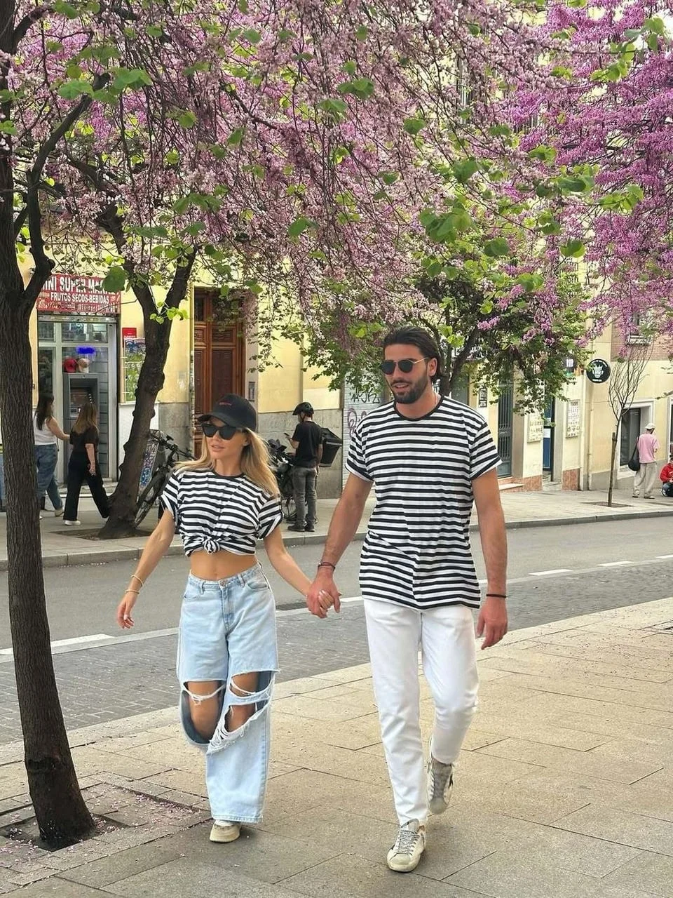 Par se drži za ruke hodajući ulicom pod rascvjetanim drvećem