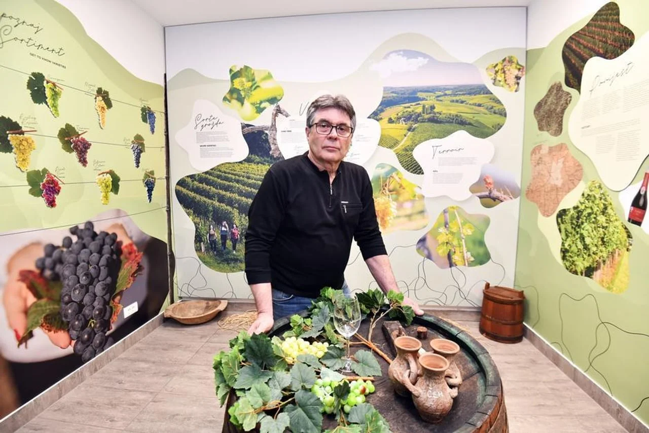 Muškarac stoji uz drvenu bačvu u edukativnom centru o vinogradarstvu.