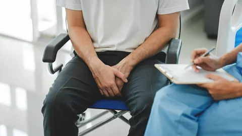 Muškarac sjedi na stolcu u liječničkoj ordinaciji dok medicinska sestra piše bilješke.